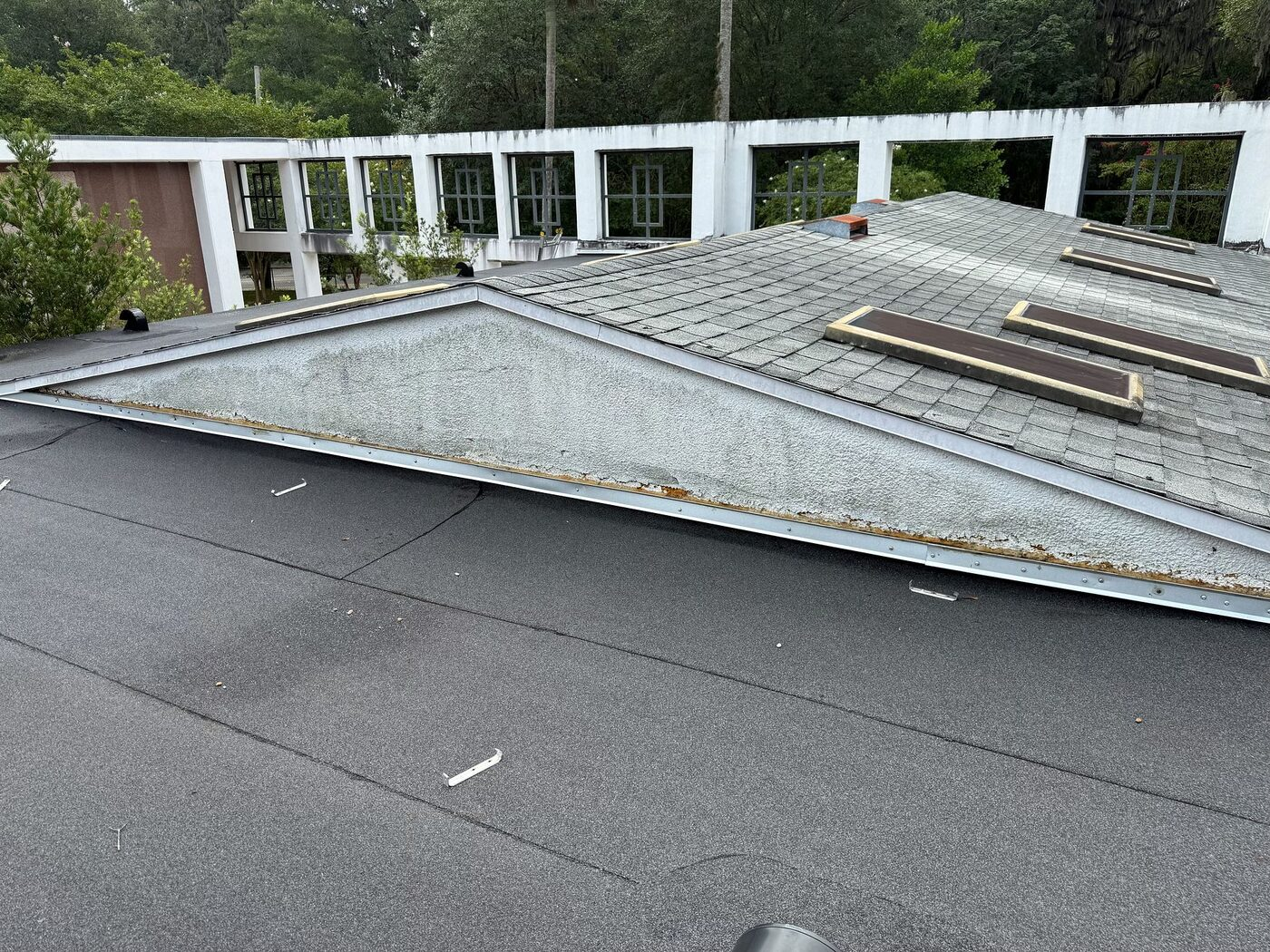 Shingle and low-slope roof sections meeting at an elevated building transition.